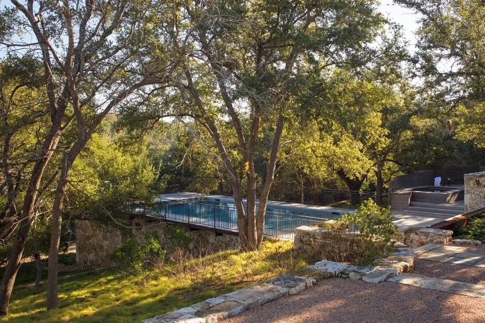 Geometric pool tucked among live oaks on a wooded hillside at golden hour in the Hill Country