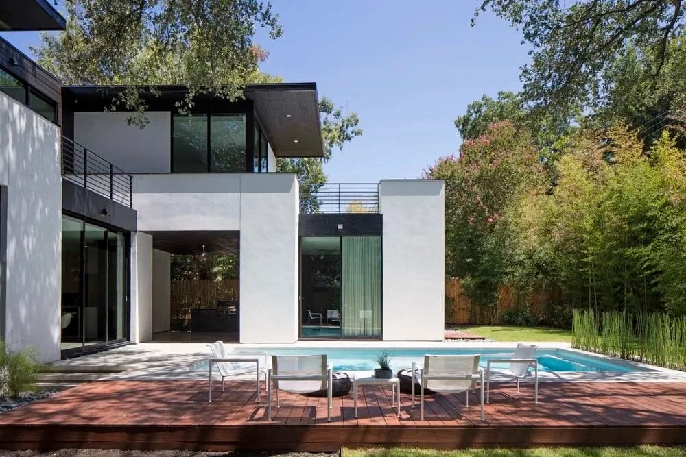 Modern white and dark stucco home with a geometric pool and patio chairs in the backyard