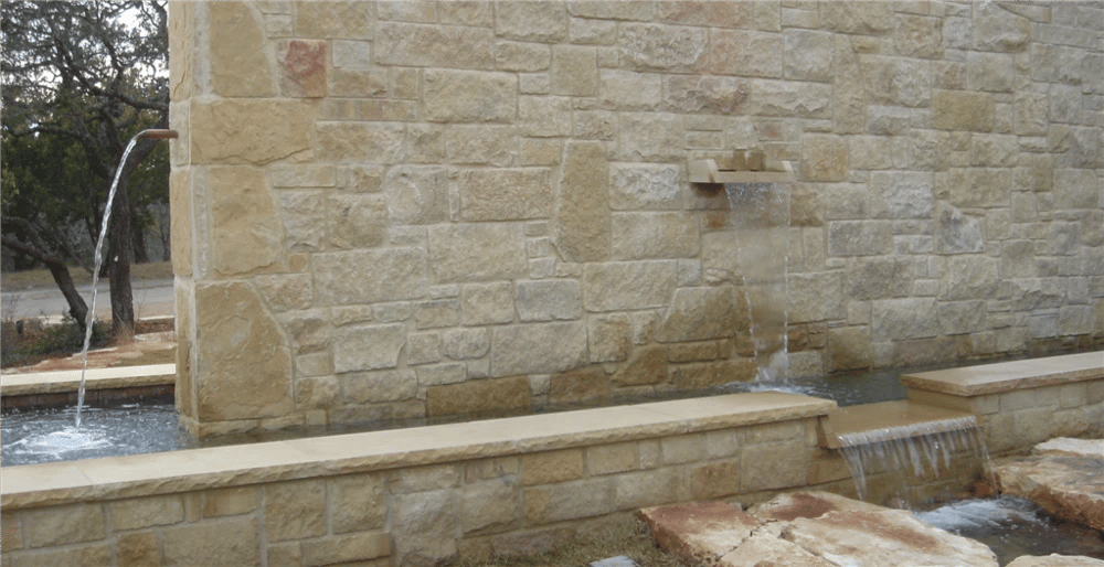 Stone wall with copper scuppers and a sheer waterfall spilling into a long limestone water trough