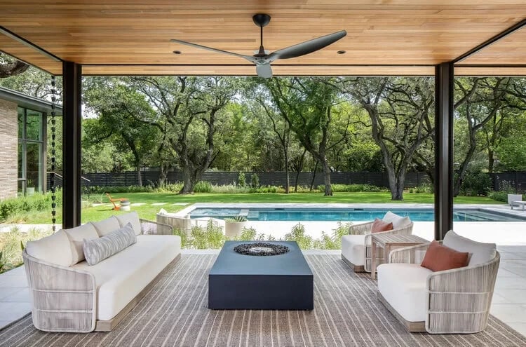 Covered patio with a wood ceiling and fire-table seating overlooking a geometric pool and wooded lawn