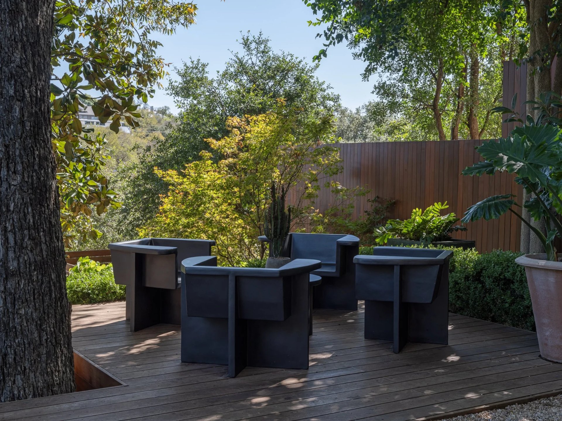 Wood deck seating with dark planter chairs around a tree, overlooking a tree-filled hillside