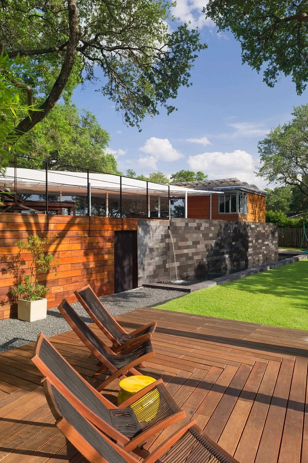 Wood deck with reclining loungers beside a cedar-clad home with a concrete-block wall and lawn