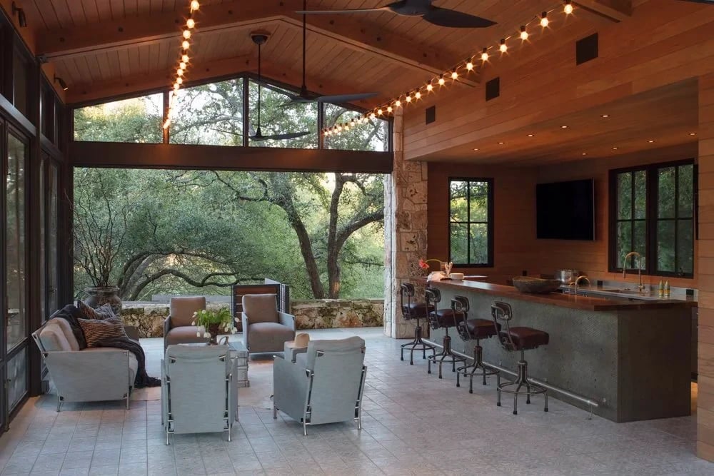 Covered outdoor kitchen and bar with string lights and oak views through tall glass walls
