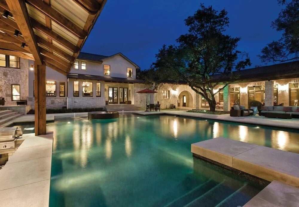 Stone courtyard pool lit at twilight, ringed by the home, covered patio, and a large oak