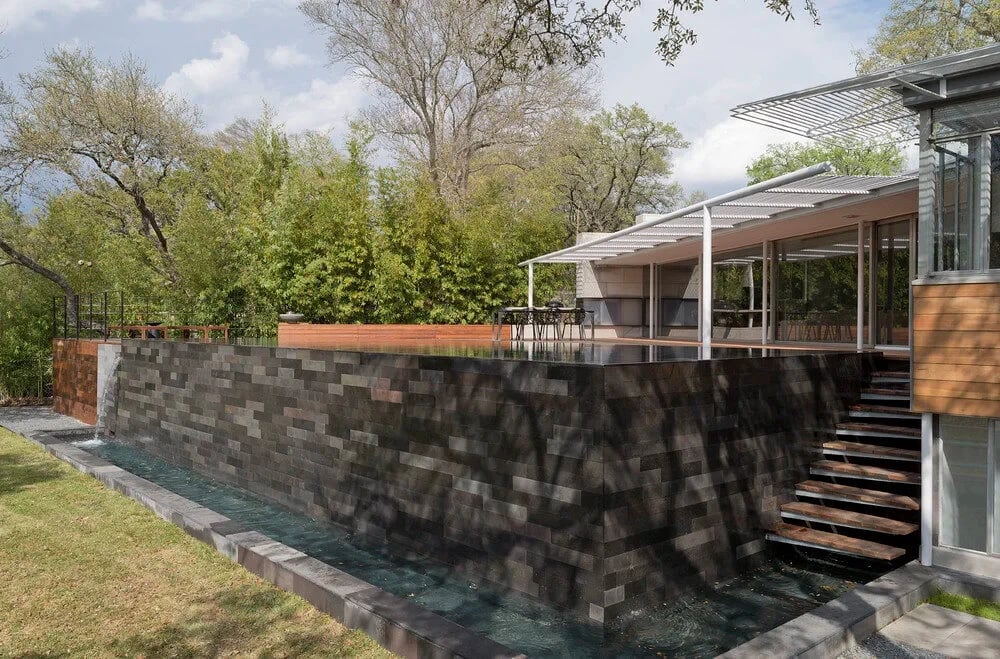 Stacked-stone retaining wall with a wood deck and steel stair above, cedar-clad home beyond