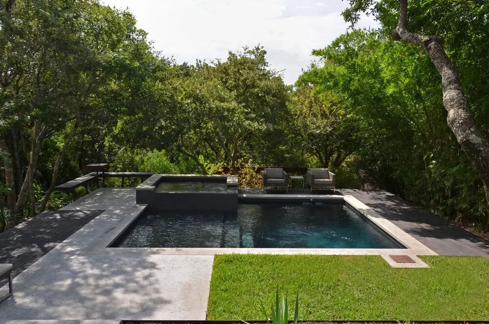 Dark geometric pool with stone coping and a grass surround backed by dense green trees