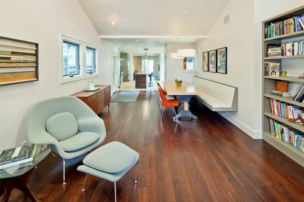 Long open living-dining space with wood floors, a built-in bench and walls of bookshelves