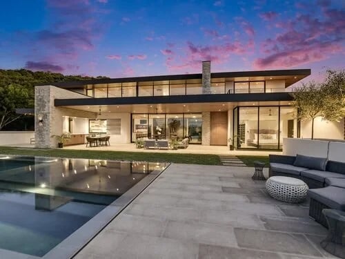 Open-plan living and dining room with stone walls and glass walls framing a twilight sky