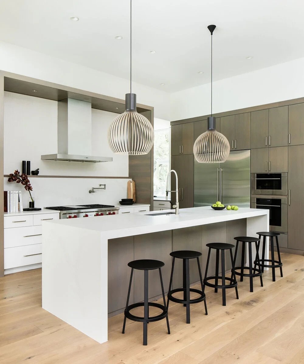 Modern kitchen with a white waterfall island, black stools and sculptural wood pendant lights
