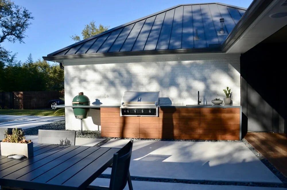 Outdoor kitchen with grill and green ceramic smoker on a white brick wall under a metal roof