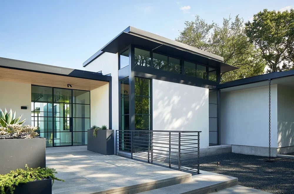 Entry of a modern home with glass walls, low roofline and a steel railing under trees