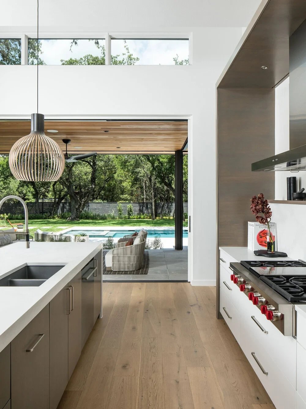 Modern kitchen with a glass door framing the backyard pool, light wood floors and a white island