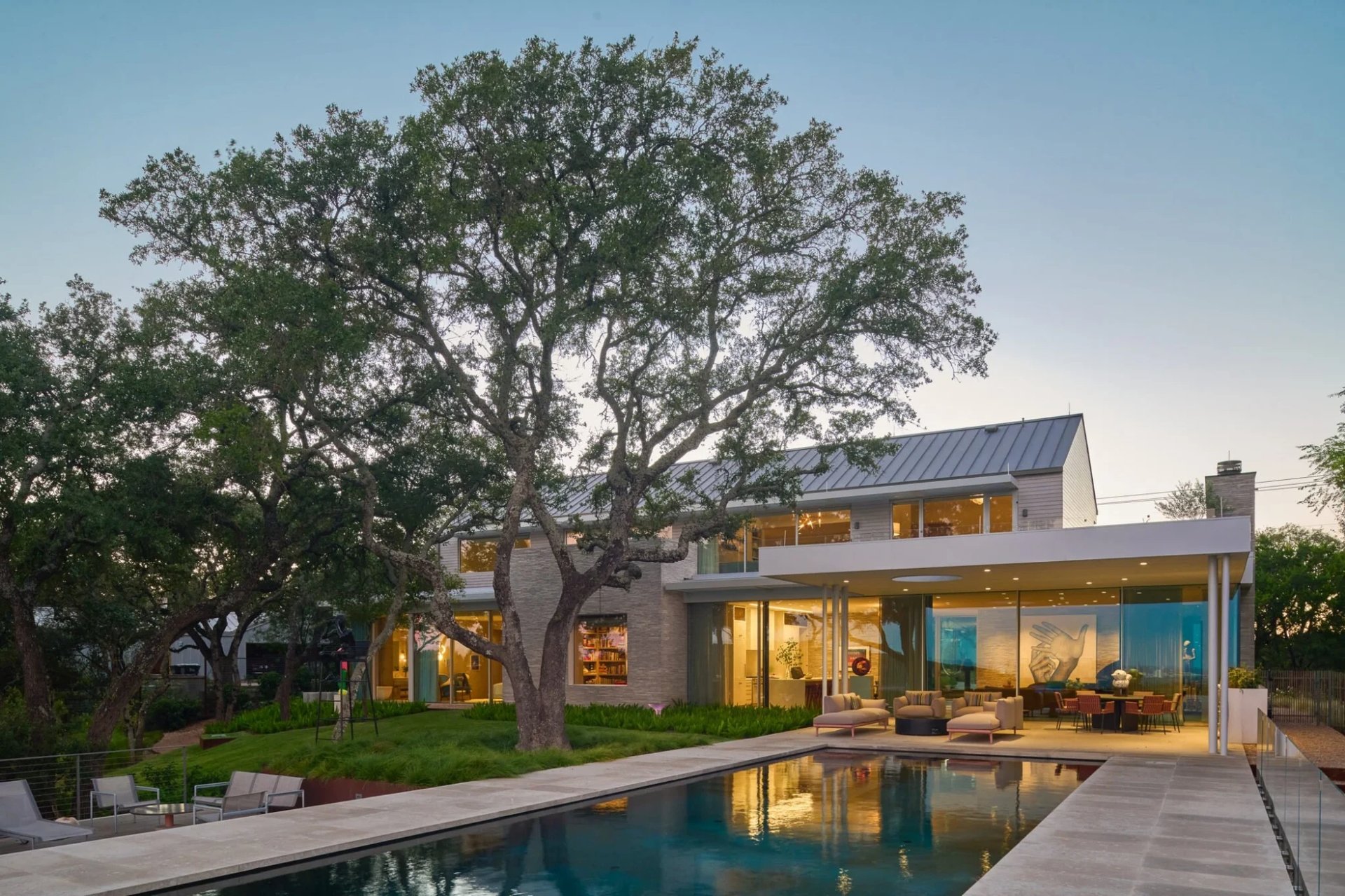 Rectangular dark infinity pool with a limestone deck and lounge chairs beside a modern home above the trees