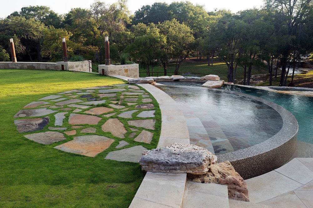 Curved negative edge pool with flagstone deck built by Modern Pools on an Austin Hill Country lot